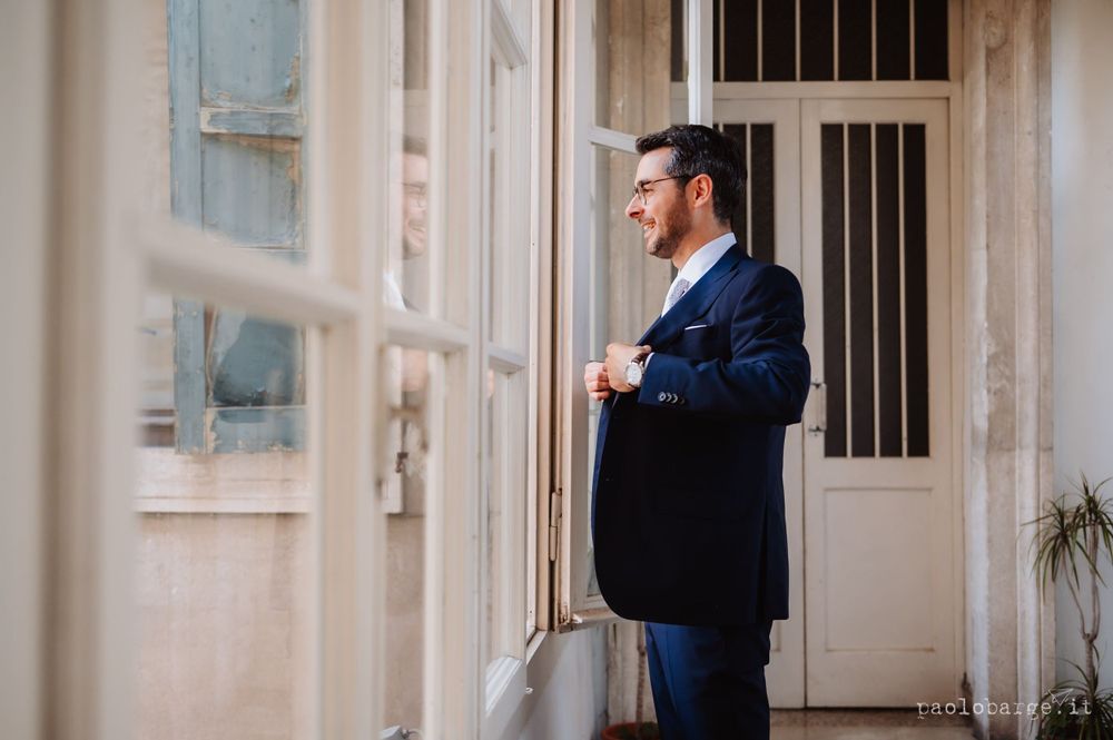 A person in a navy suit stands contemplatively by white columns and walls.