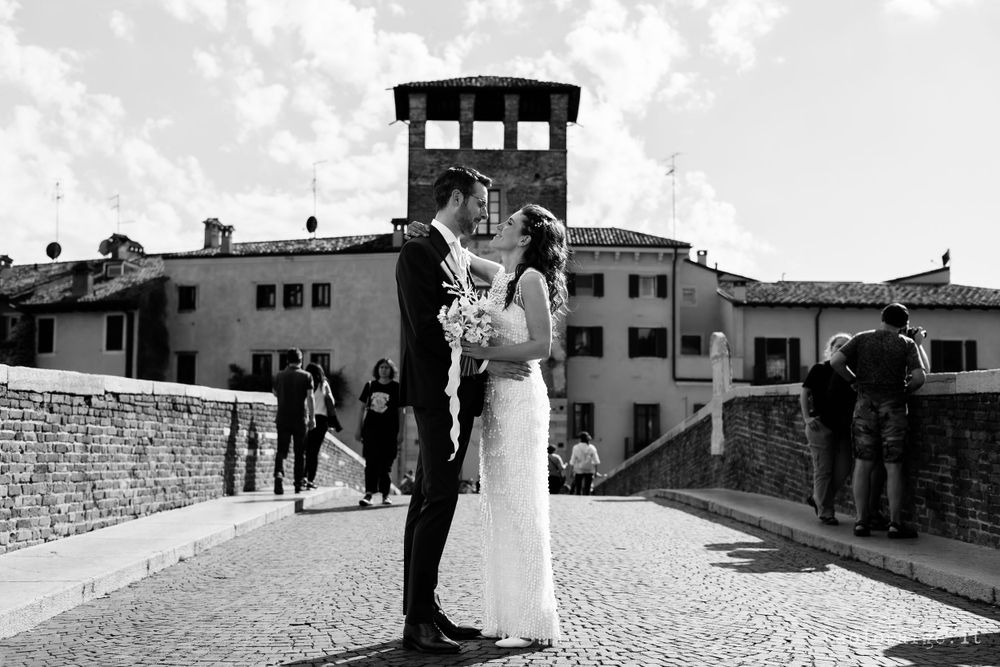 Black and white photo of a wedding couple on a historic stone bridge with architecture in the background.