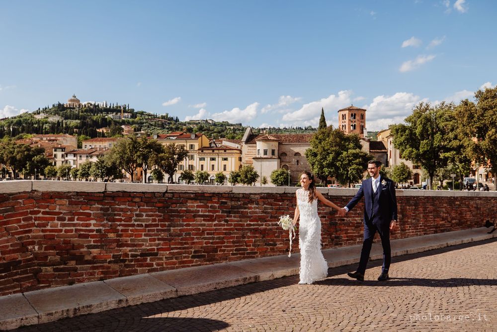 Couple walking along ancient brick wall with scenic Italian landscape and architecture behind them.