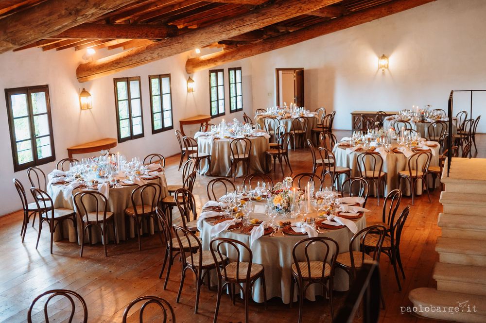 Elegant rustic wedding reception venue with wooden tables and chairs set for dining under exposed beams.