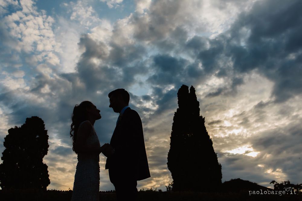 Silhouettes of tall cypress trees and figures against a dramatic sunset sky.