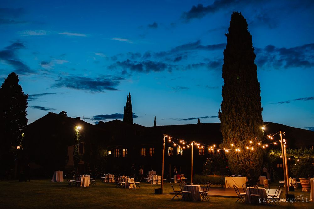 Evening outdoor venue with string lights illuminating cypress trees against a deep blue sky.