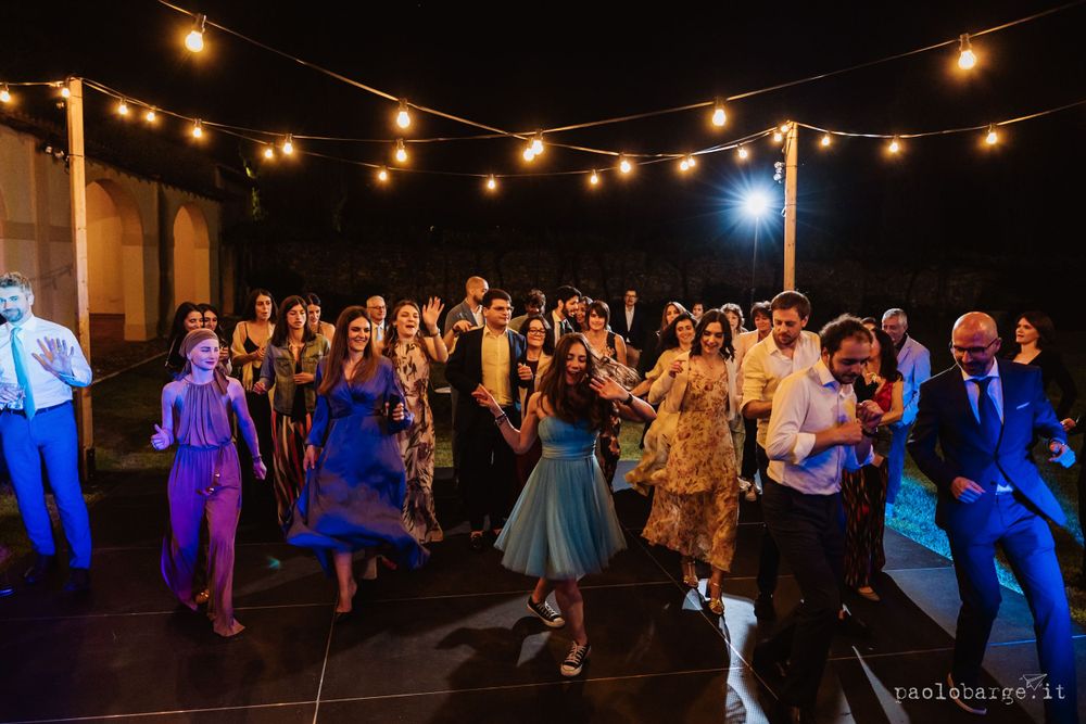 Wedding guests dancing and celebrating on an outdoor dance floor lit by string lights.
