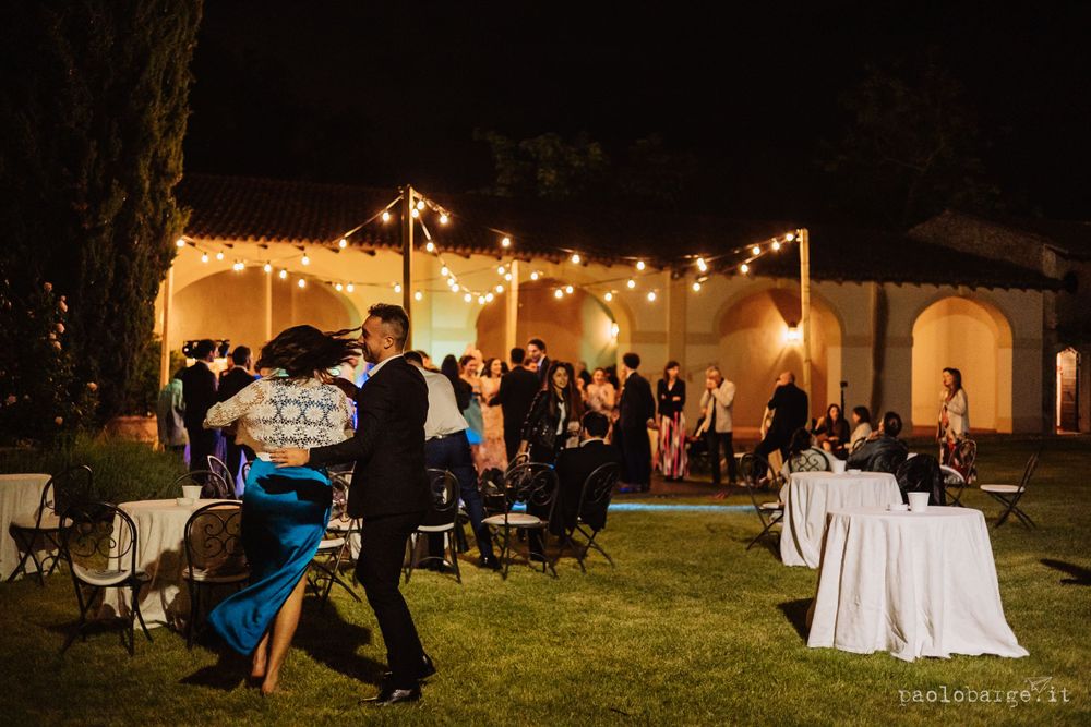 Outdoor evening wedding reception with string lights illuminating dancers on a lawn.