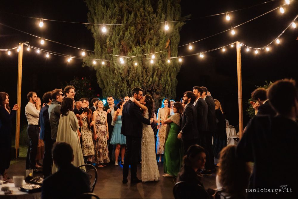 Evening wedding reception with couples dancing under strung cafe lights and trees.