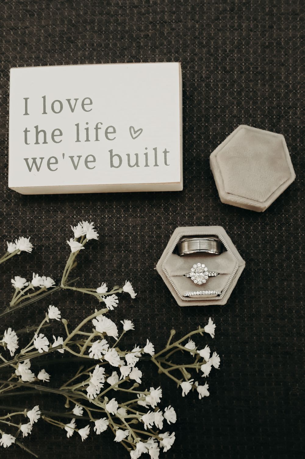 Wedding details flatlay with rings, delicate white flowers and a sign reading 'I love the life we've built'.
