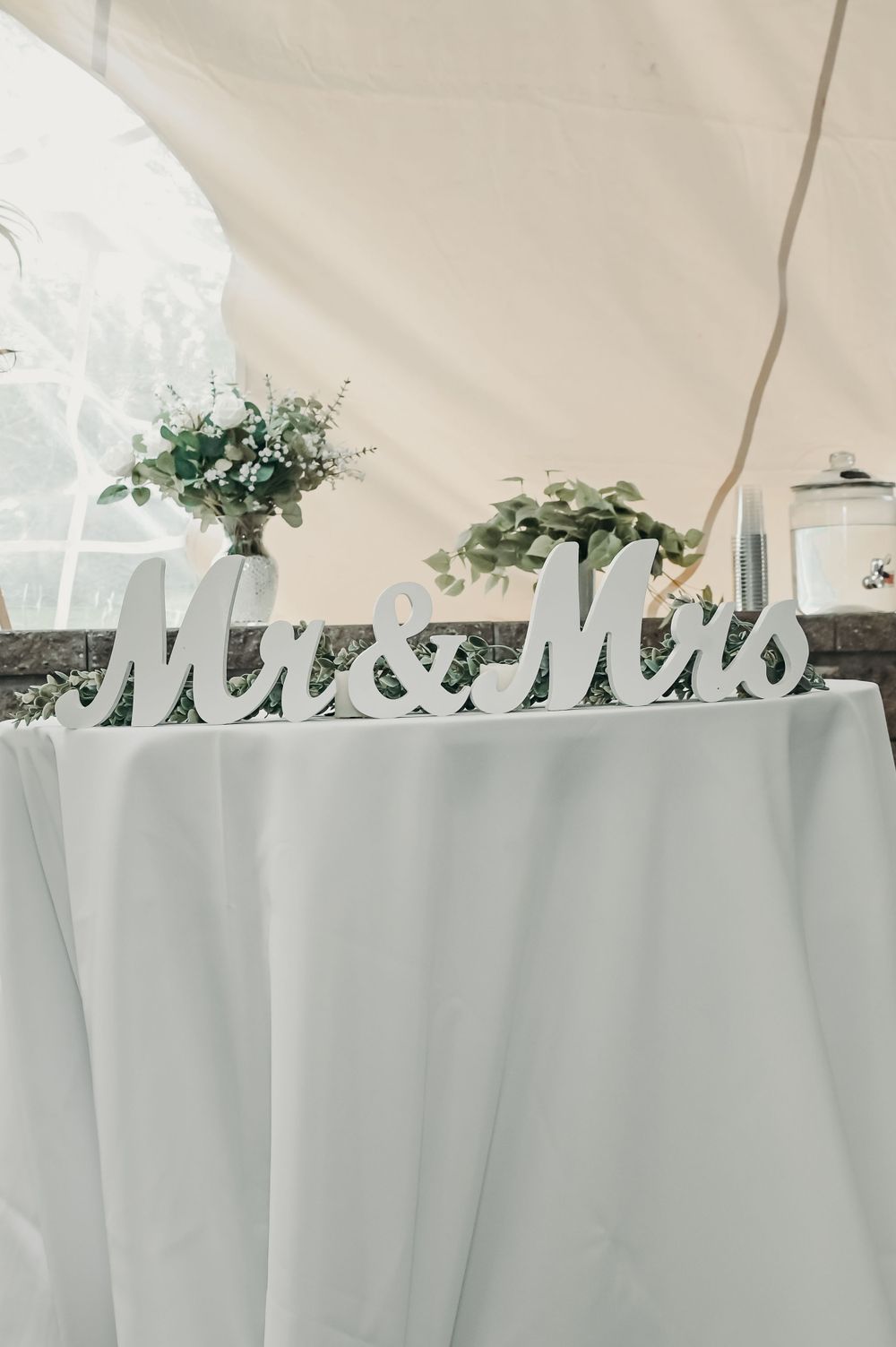 White 'Mr & Mrs' sign displayed on reception table with floral arrangements.