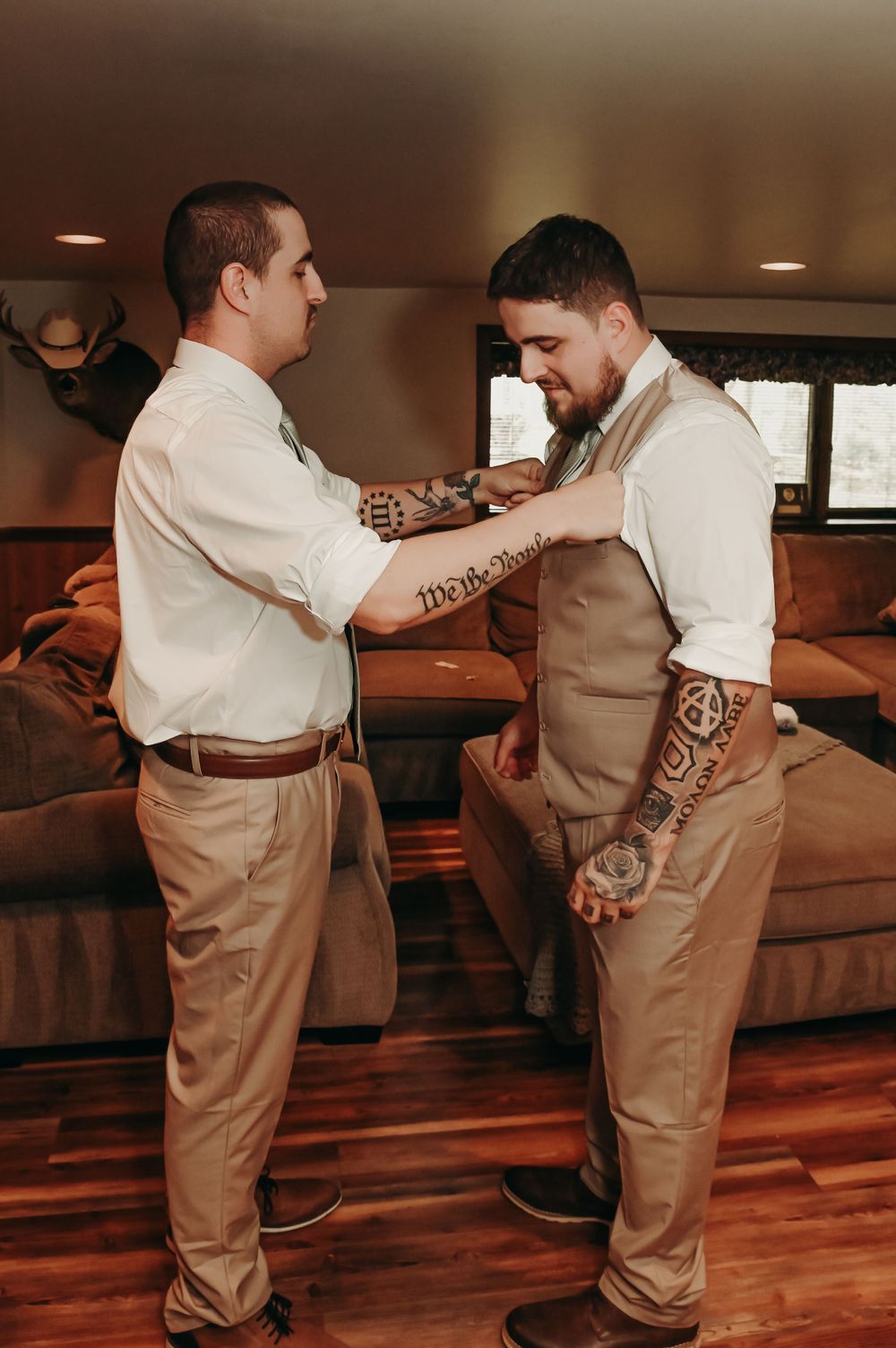 Two people in formal attire help each other adjust clothing and accessories before an event.