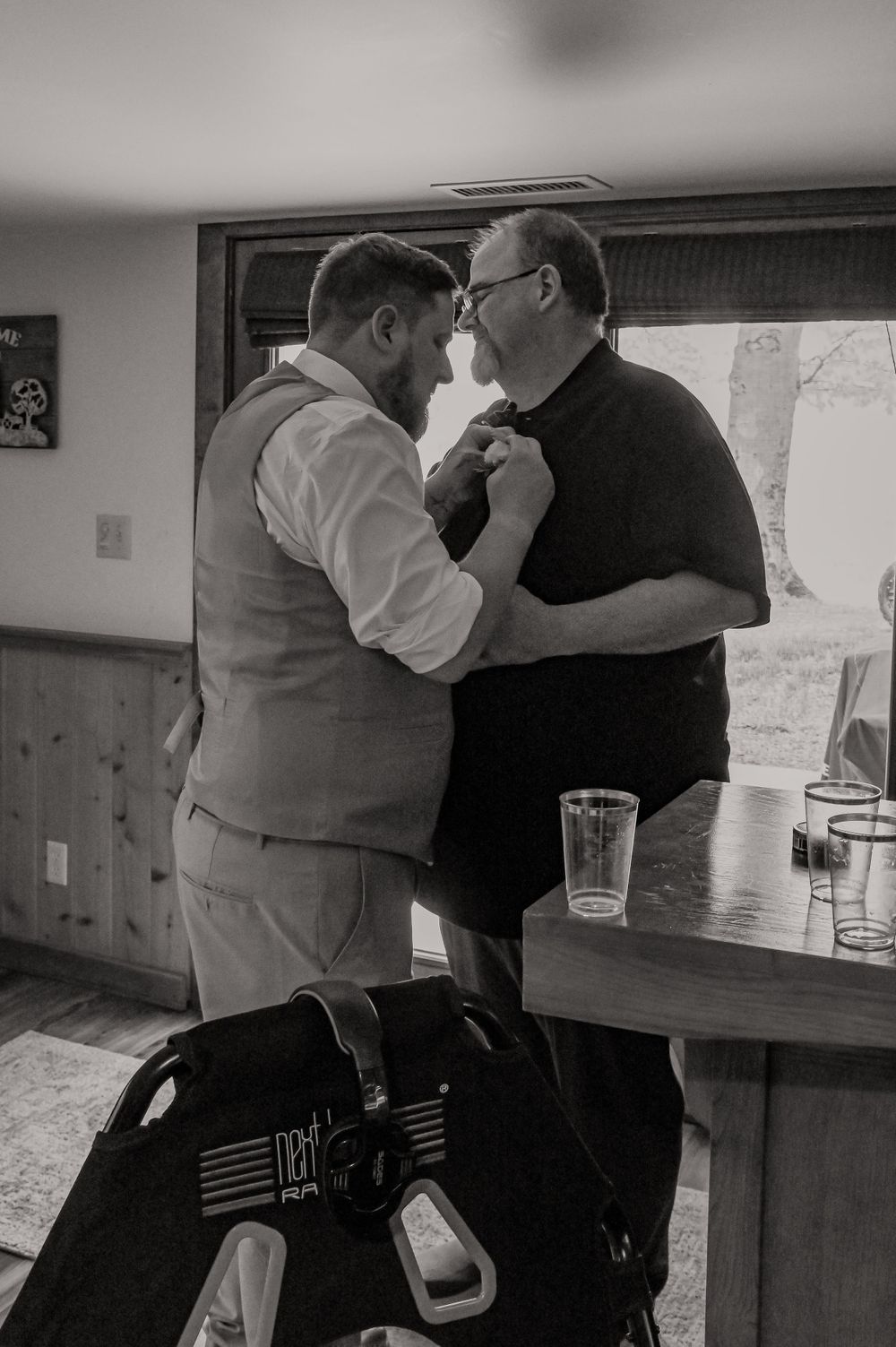 Wedding party members assist each other with adjusting formal attire indoors.