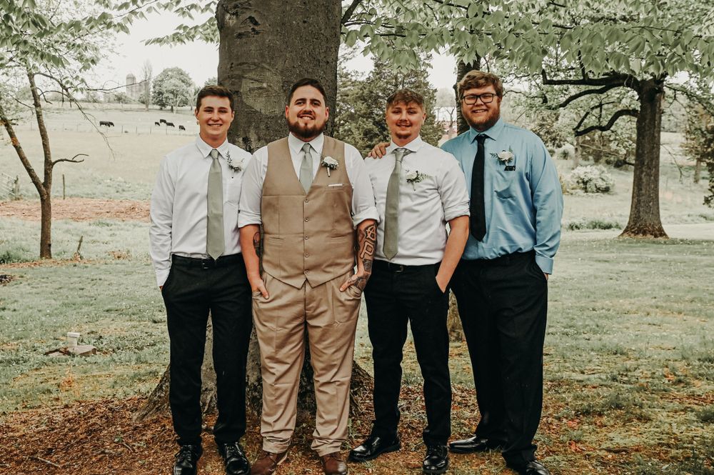 Group photo of wedding party members wearing tan suits and formal attire outdoors.