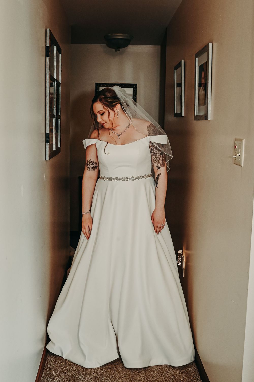 Elegant white wedding gown with cap sleeves and crystal belt detail in a hallway setting.