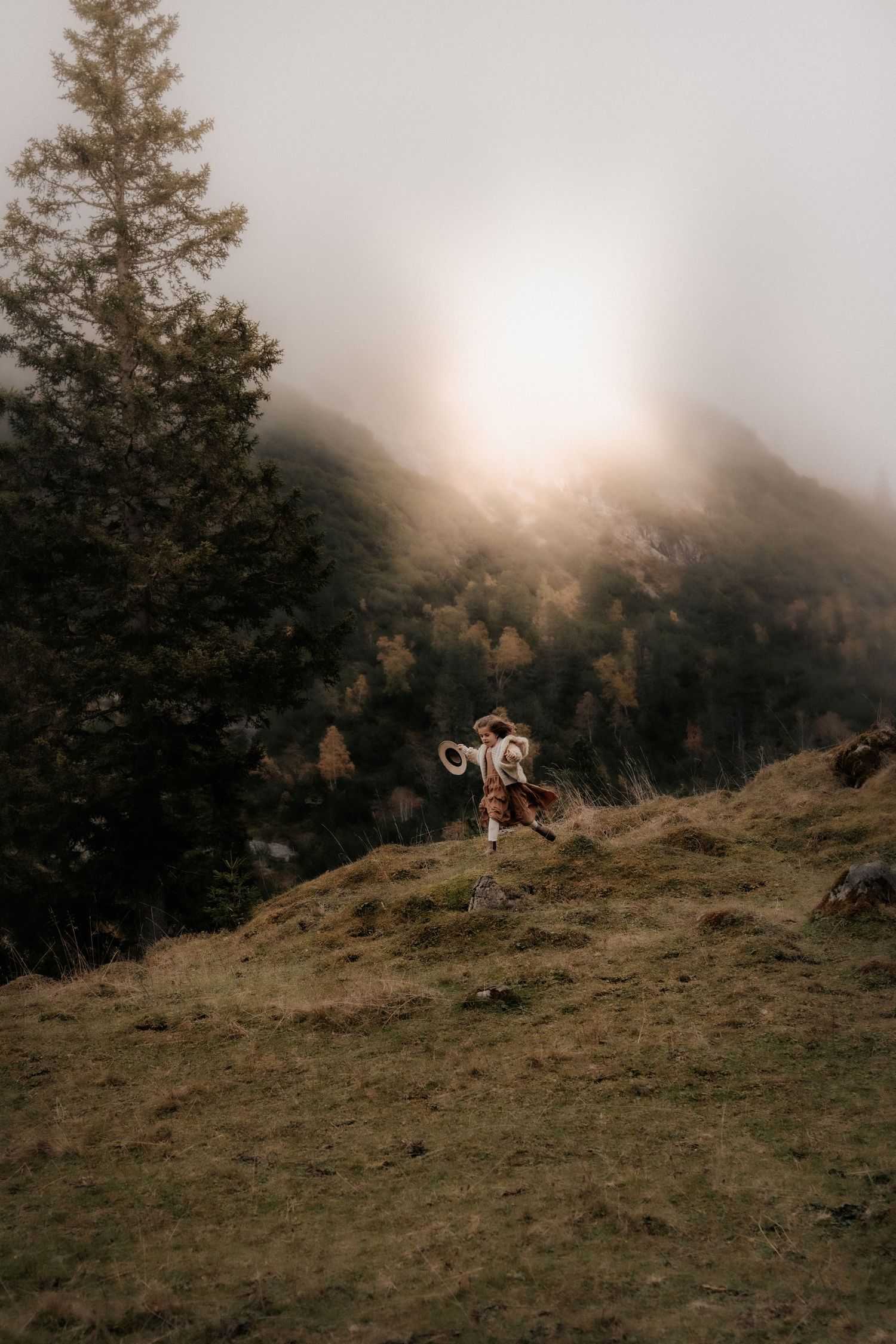 Silhouette of person dancing on hillside against misty mountain sunset.
