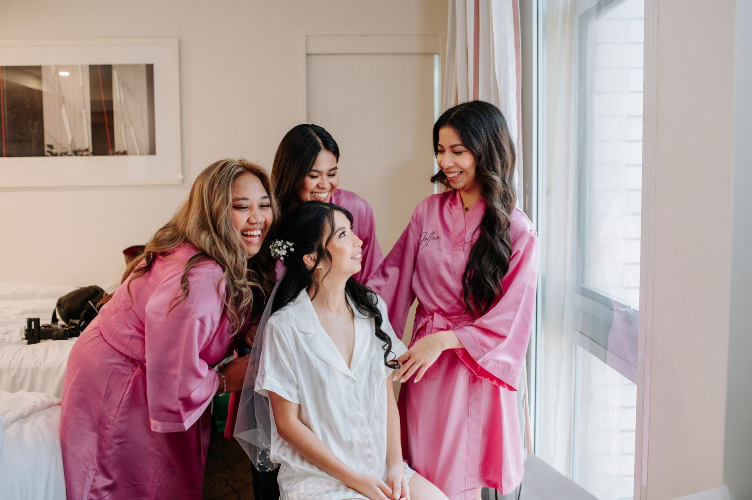 Bridal party in pink robes sharing a light moment during wedding preparations.