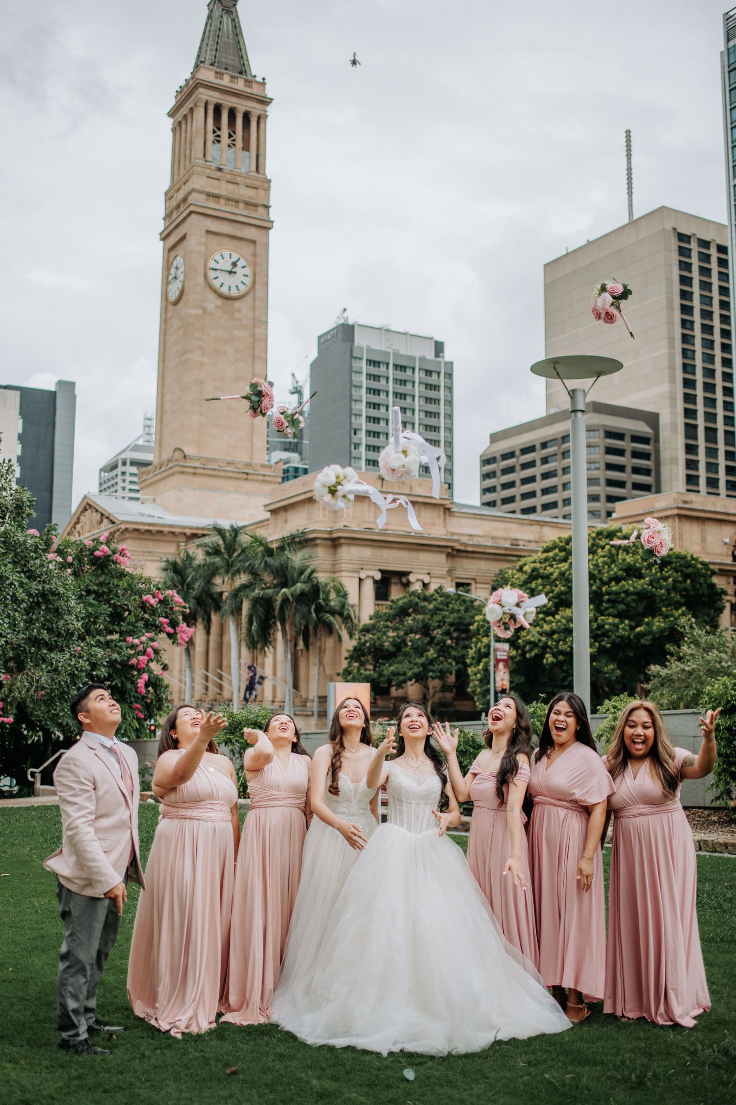 Wedding party in blush pink dresses posing in front of Brisbane City Hall with decorative balloons.