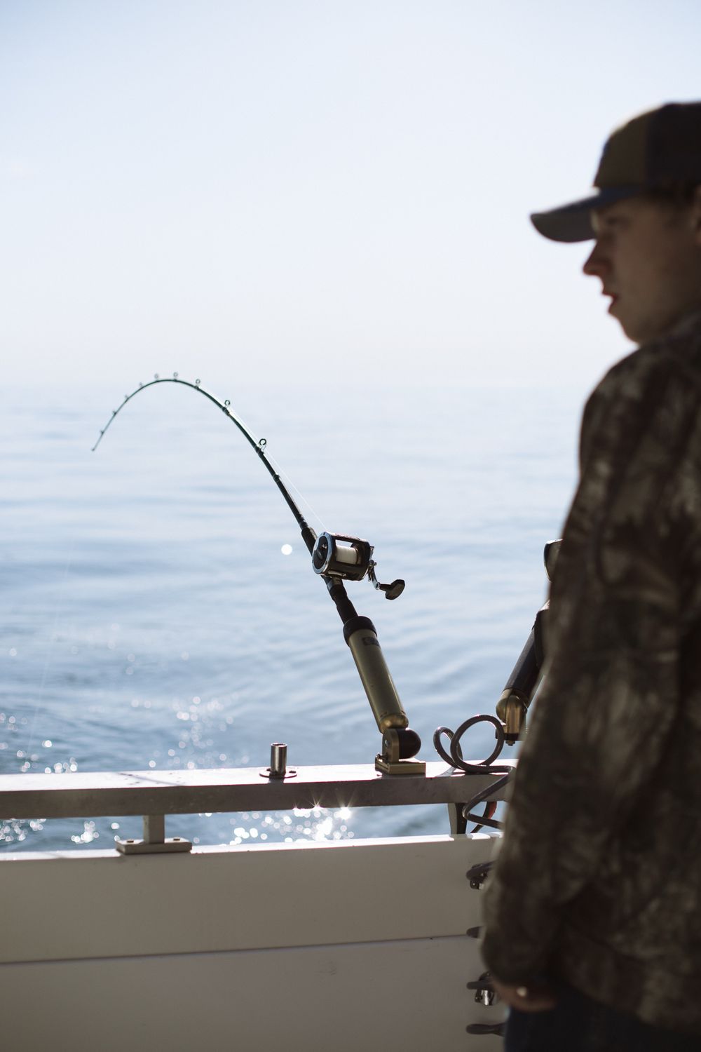 man standing next to fishing rod on back of large boat in lake michigan