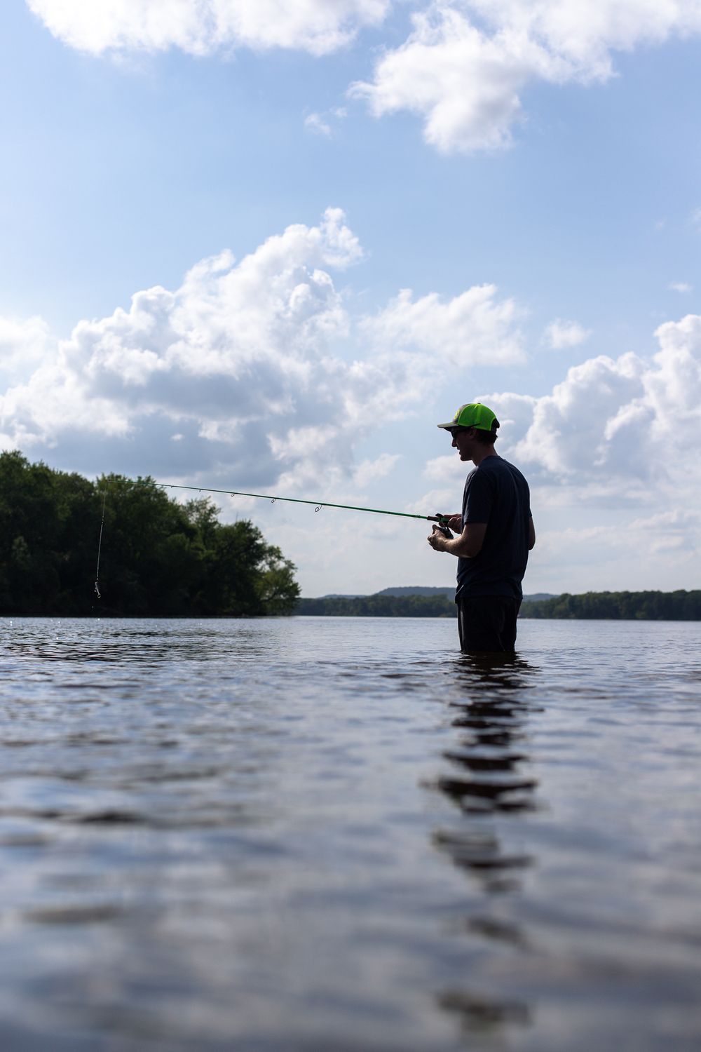 man standing in water in wisconsin river holding fishing rod with line in water