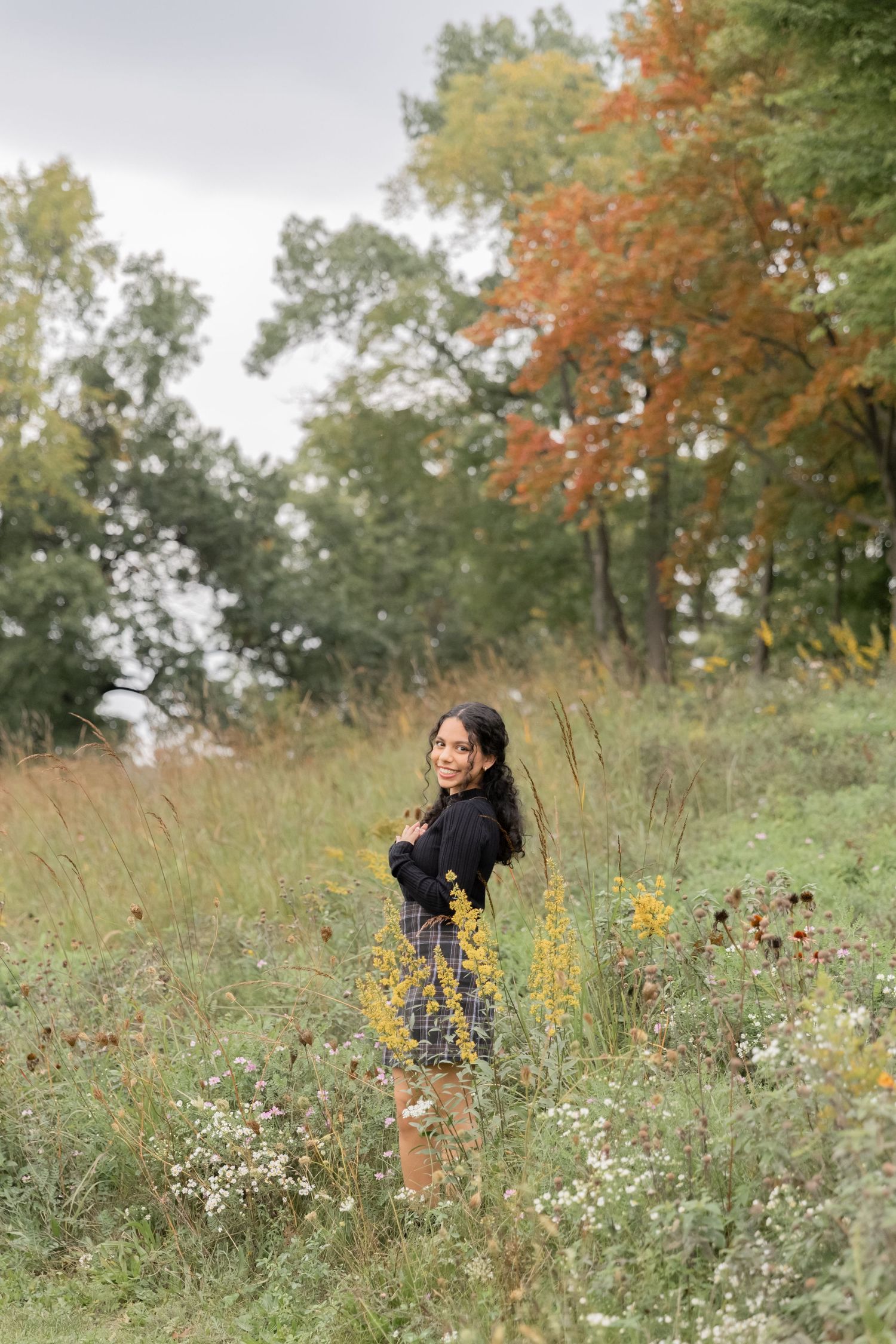 teenage girl standing in a wildflower field in front of a orange tree in october