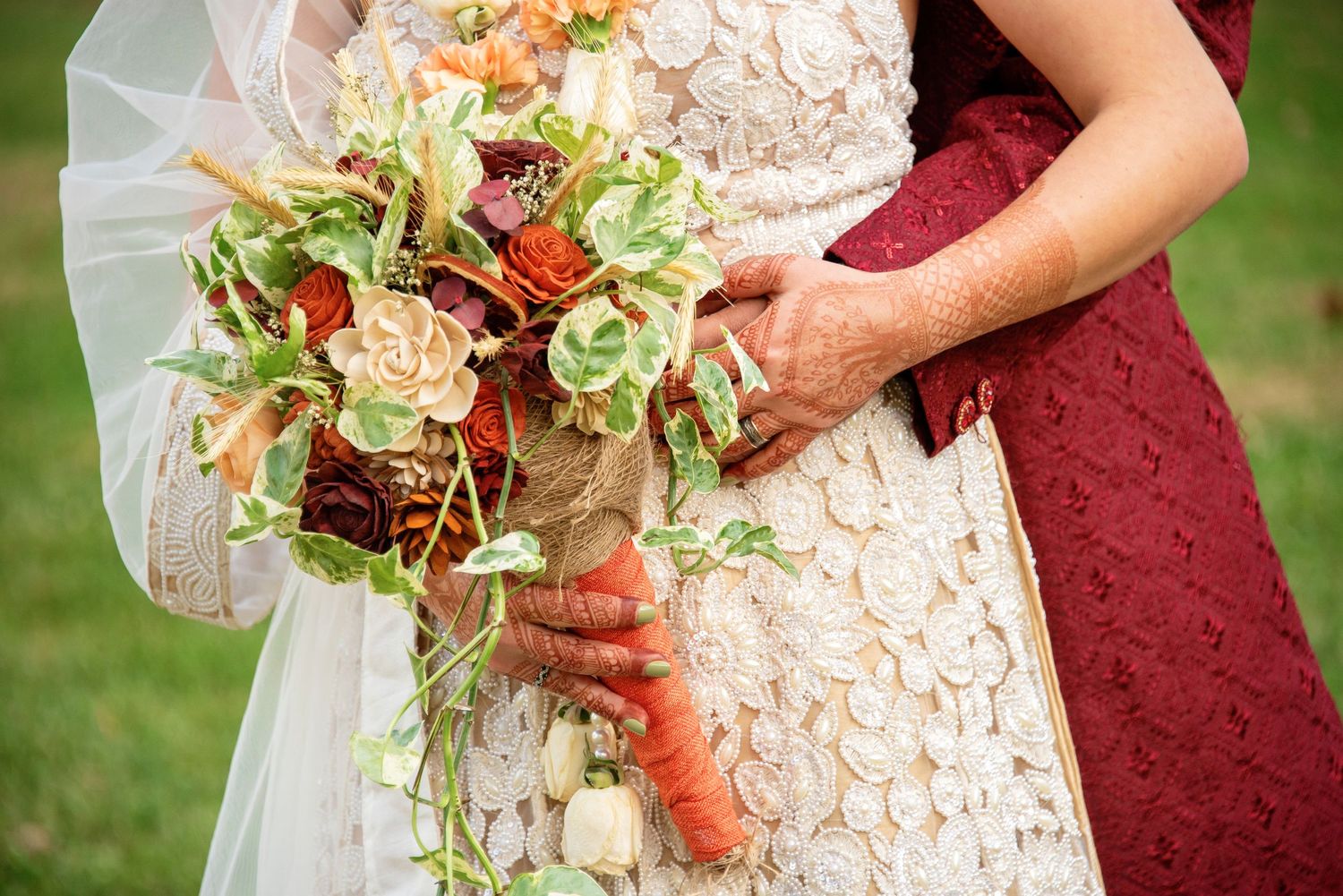 Close up of ornate wedding bouquet with cascading greenery and flowers held against lace dress.