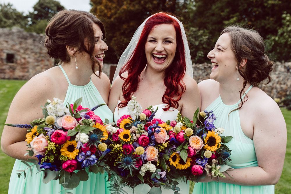 Bridesmaids in mint green dresses hold vibrant sunflower and wildflower bouquets at an outdoor wedding.