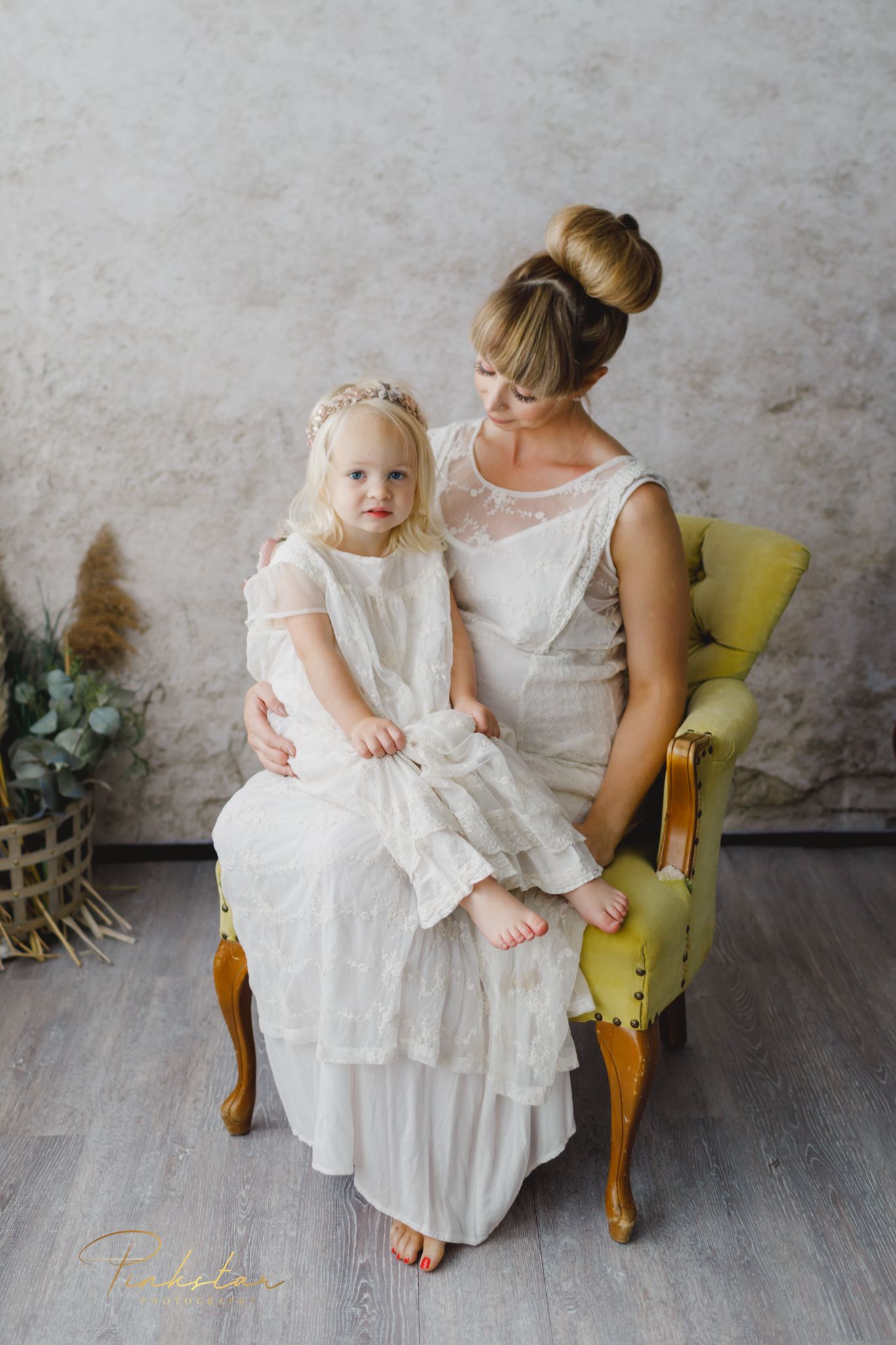 A sweet bonding moment in white dresses against a rustic wall with vintage yellow chair.