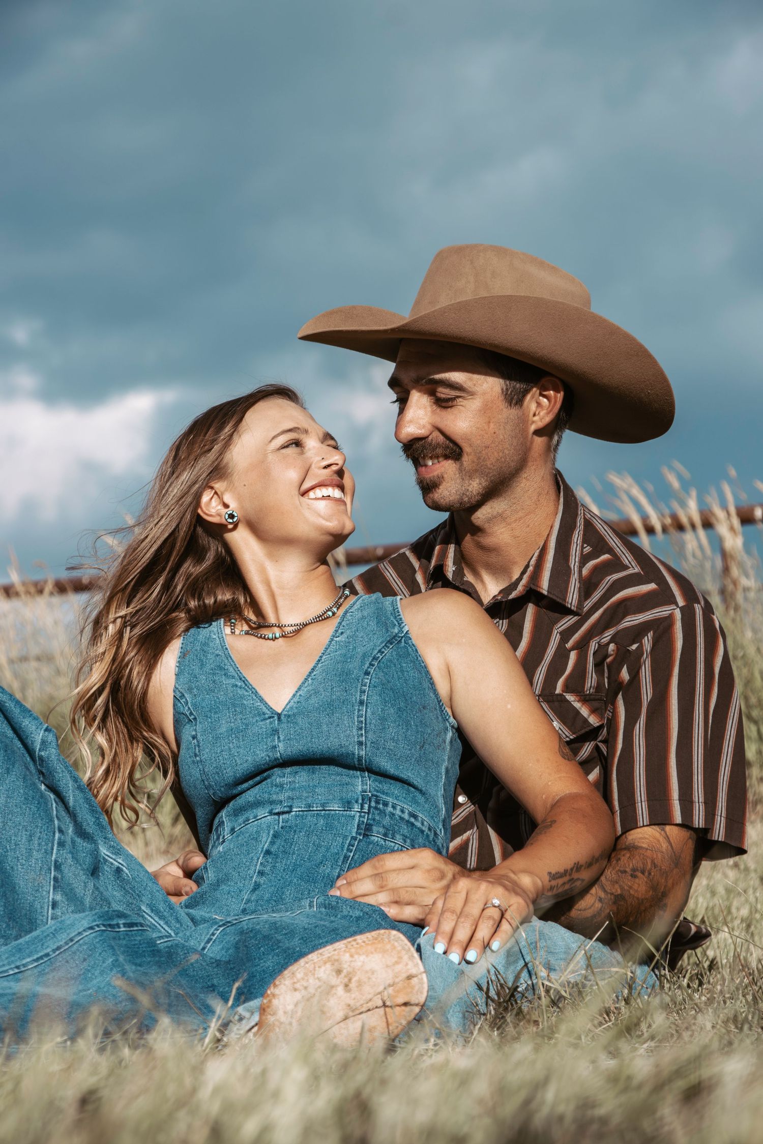 Couple sharing an intimate moment in a rustic field with mountains visible in the distance.