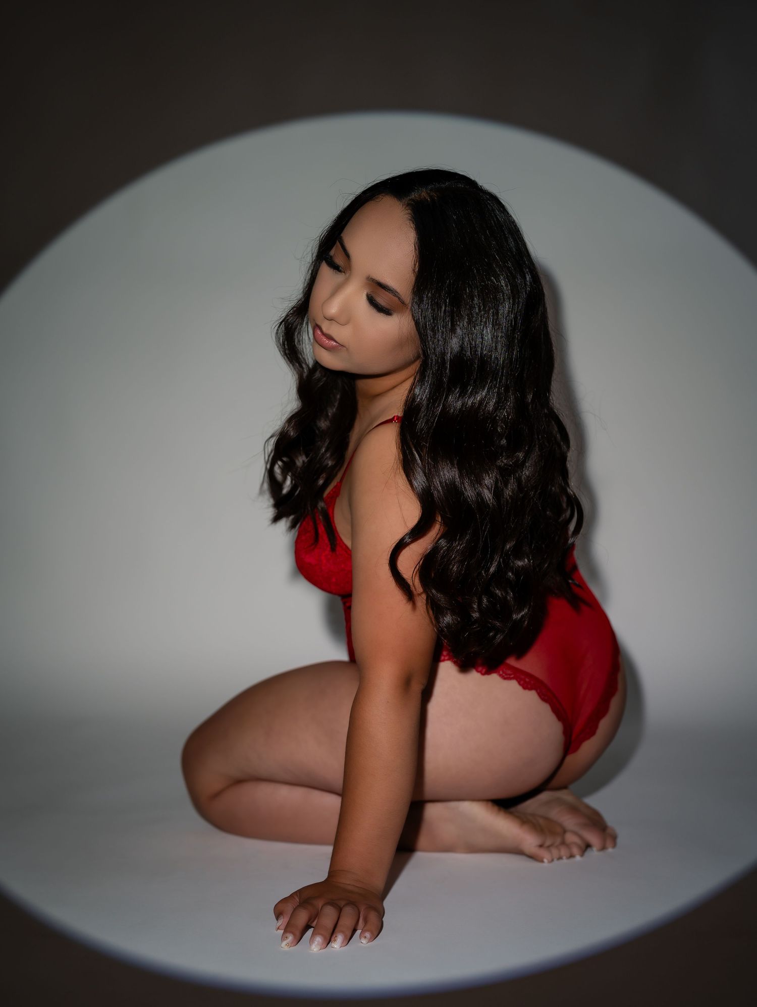 Dramatic boudoir photography with spotlight effect and red lingerie.