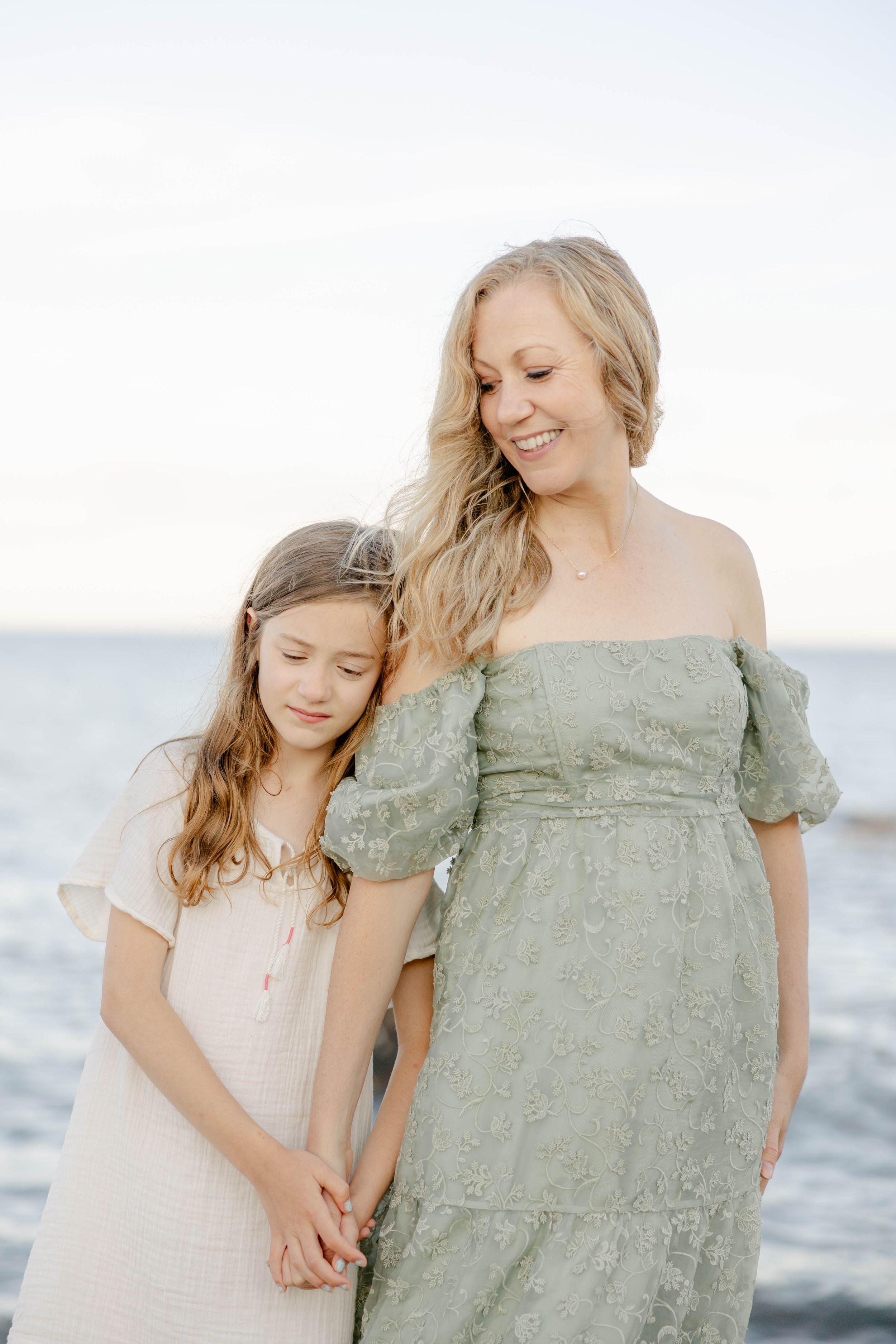 Two people in flowing dresses stand together by the ocean at sunset. Newborn photography session in Connecticut studio by Ashley Nielsen Stu