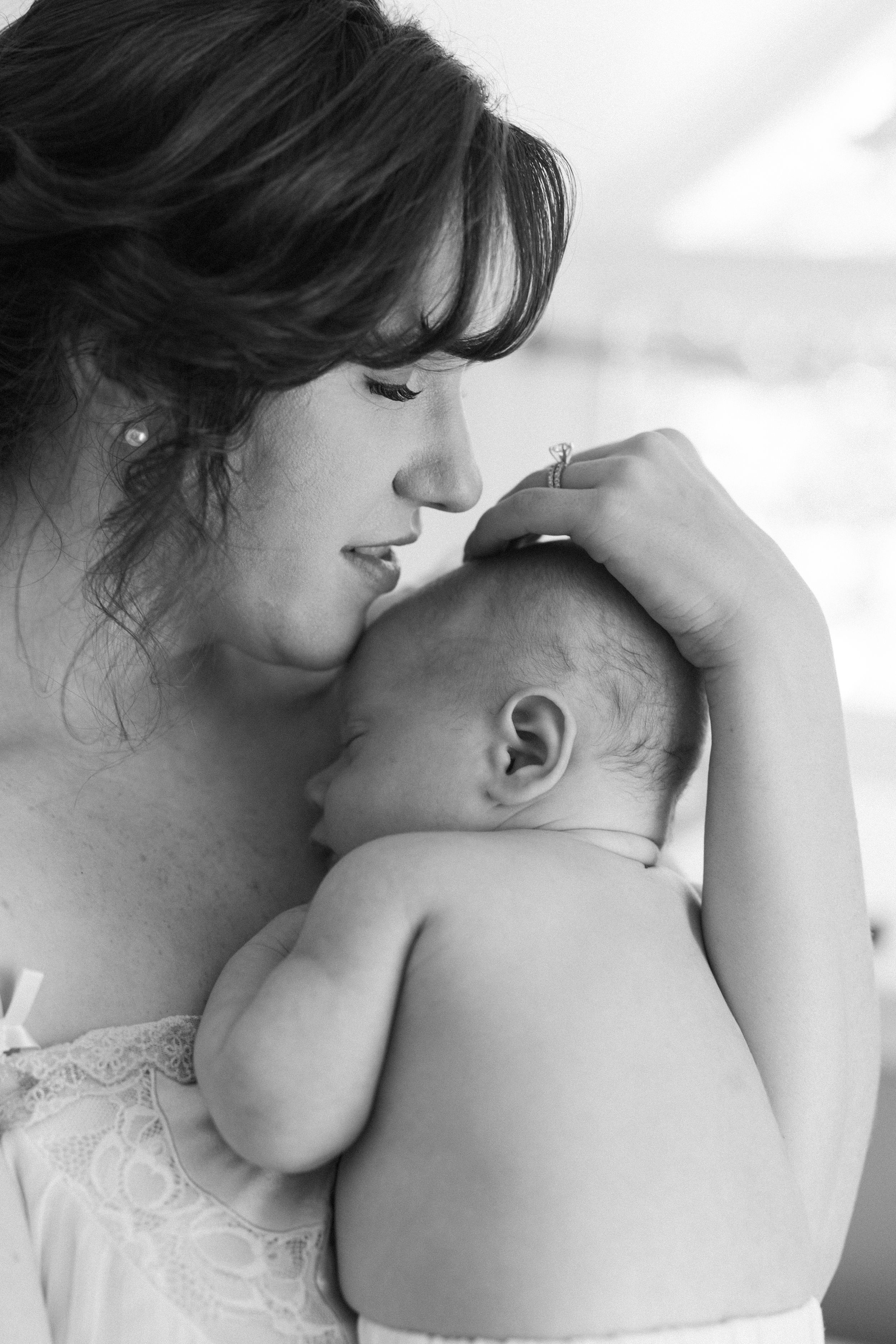 Black and white photo of a mother tenderly holding and kissing her newborn baby.