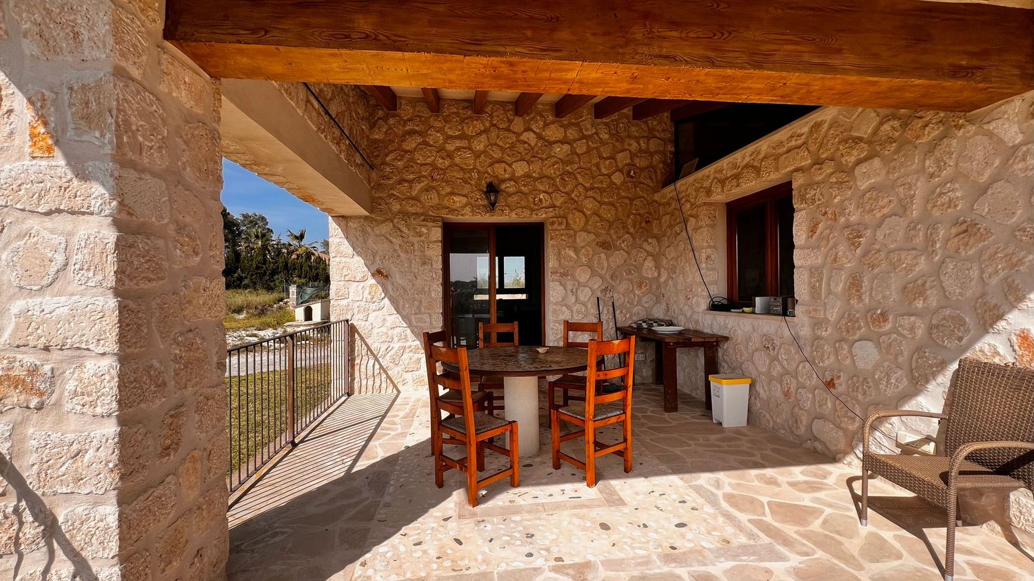 Stone villa covered patio with wooden dining table and chairs, rustic Mediterranean outdoor living space with scenic countryside views.