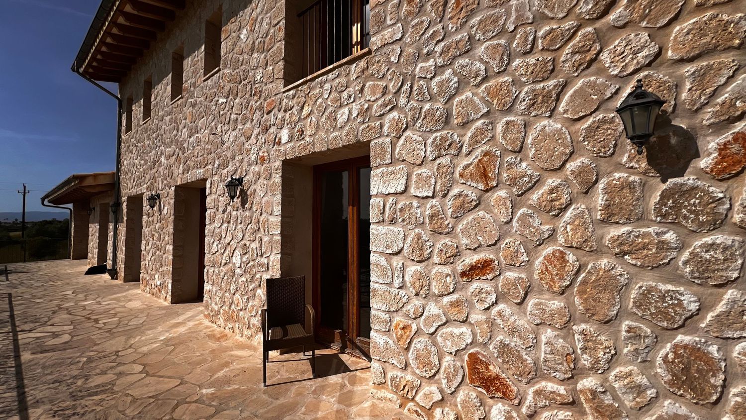 Rustic stone exterior wall of a traditional countryside villa with wooden door and wall-mounted lantern.
