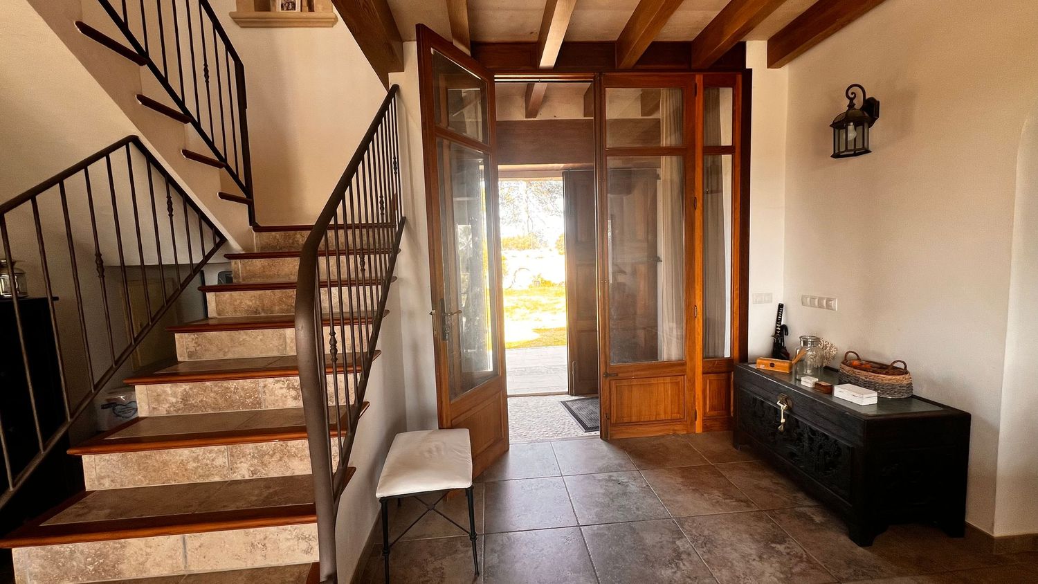 Elegant home entryway featuring wooden staircase, tiled floor, glass front door, and antique sideboard.