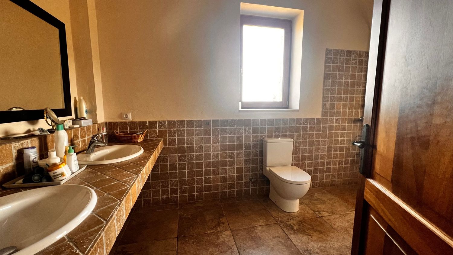 Elegant bathroom with dual sinks, tiled walls, a toilet, and a small window providing natural light.