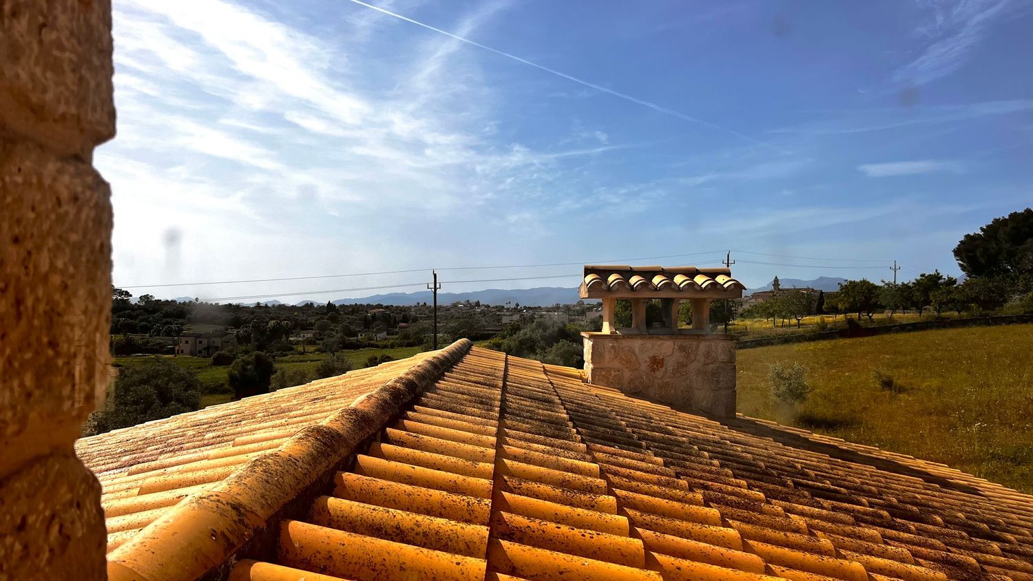 Traditional terracotta tiled rooftop with panoramic countryside and sea views under a blue sky.
