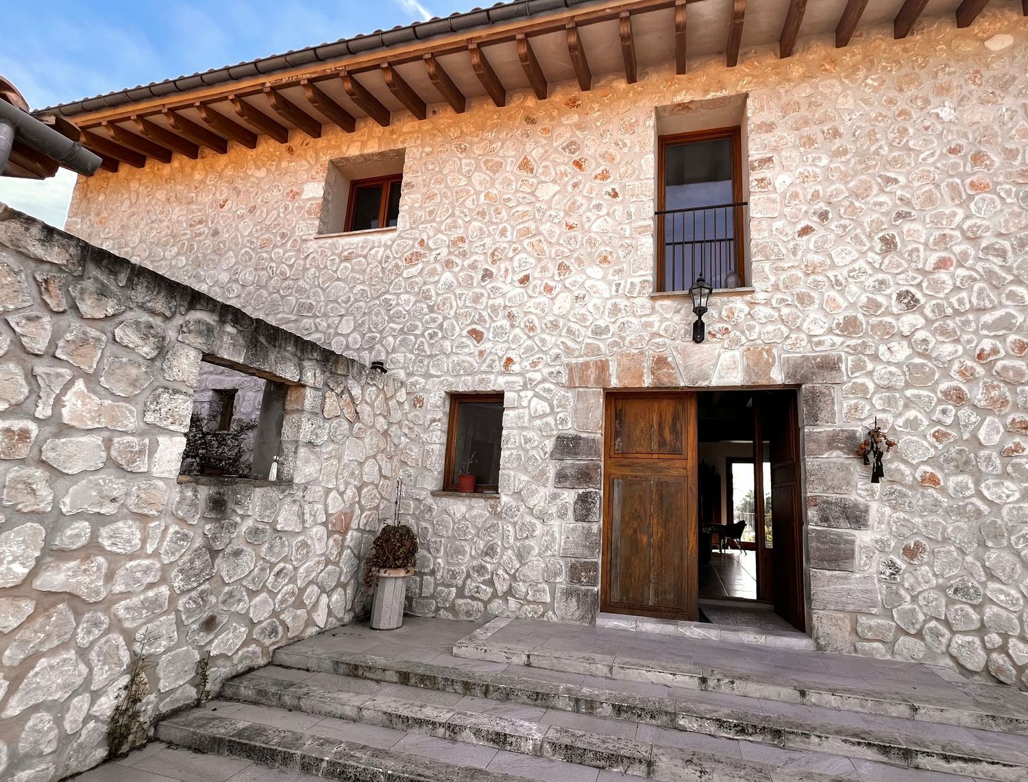 Rustic stone farmhouse exterior with wooden door, steps, and small windows in a traditional rural architectural style.