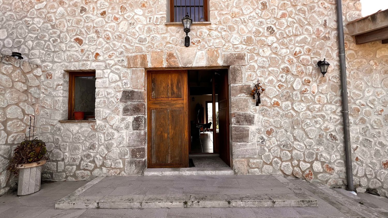 Rustic stone building exterior featuring a wooden door, small window, and wall-mounted lantern in a traditional architectural style.
