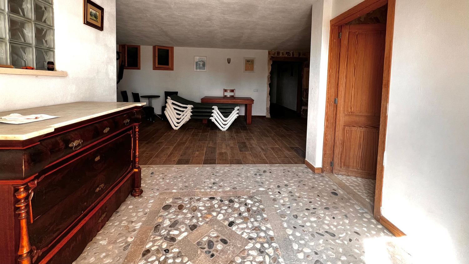 Spacious living room with hardwood floors, patterned tile entryway, wooden dresser, and a dining area with wooden door.
