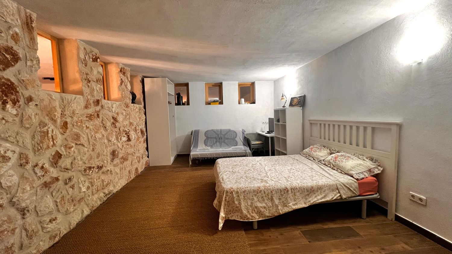 Rustic bedroom with stone accent wall, hardwood floors, two beds with floral bedding, and soft ambient lighting.