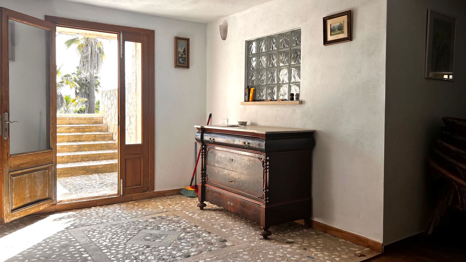 Bright entryway with wooden dresser, tiled floor, and glass door leading to a sunny outdoor area.