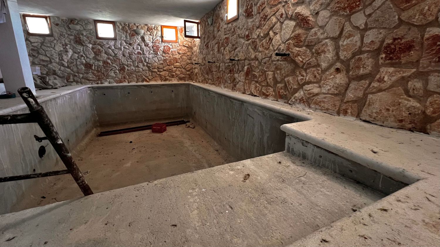 Stone-walled underground cistern with concrete basin, steps, and small windows in a historic building.