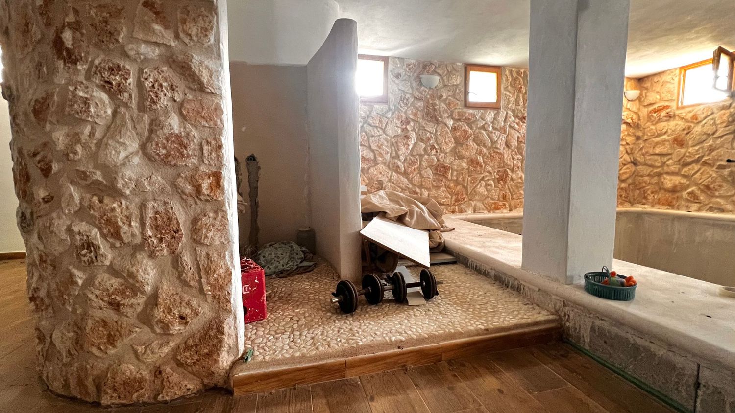 Rustic stone interior spa room with decorative carved column, pebble floor, and traditional hammam-style seating areas.