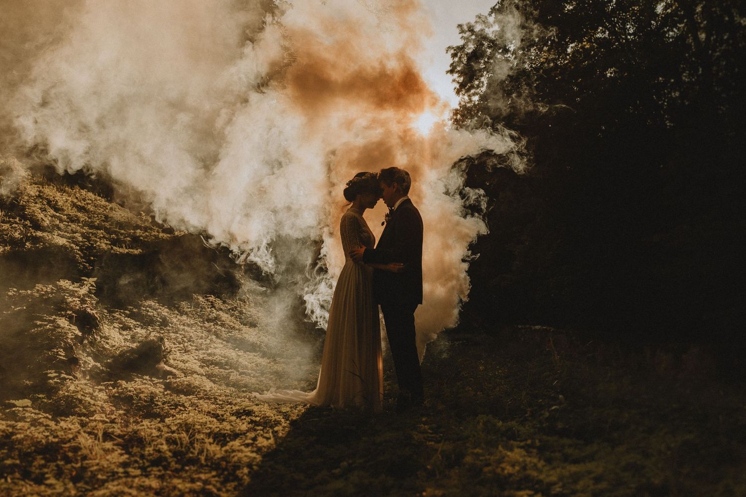 Bride and groom in Santorini embracing and touching foreheads with volcanic smoke behind them
