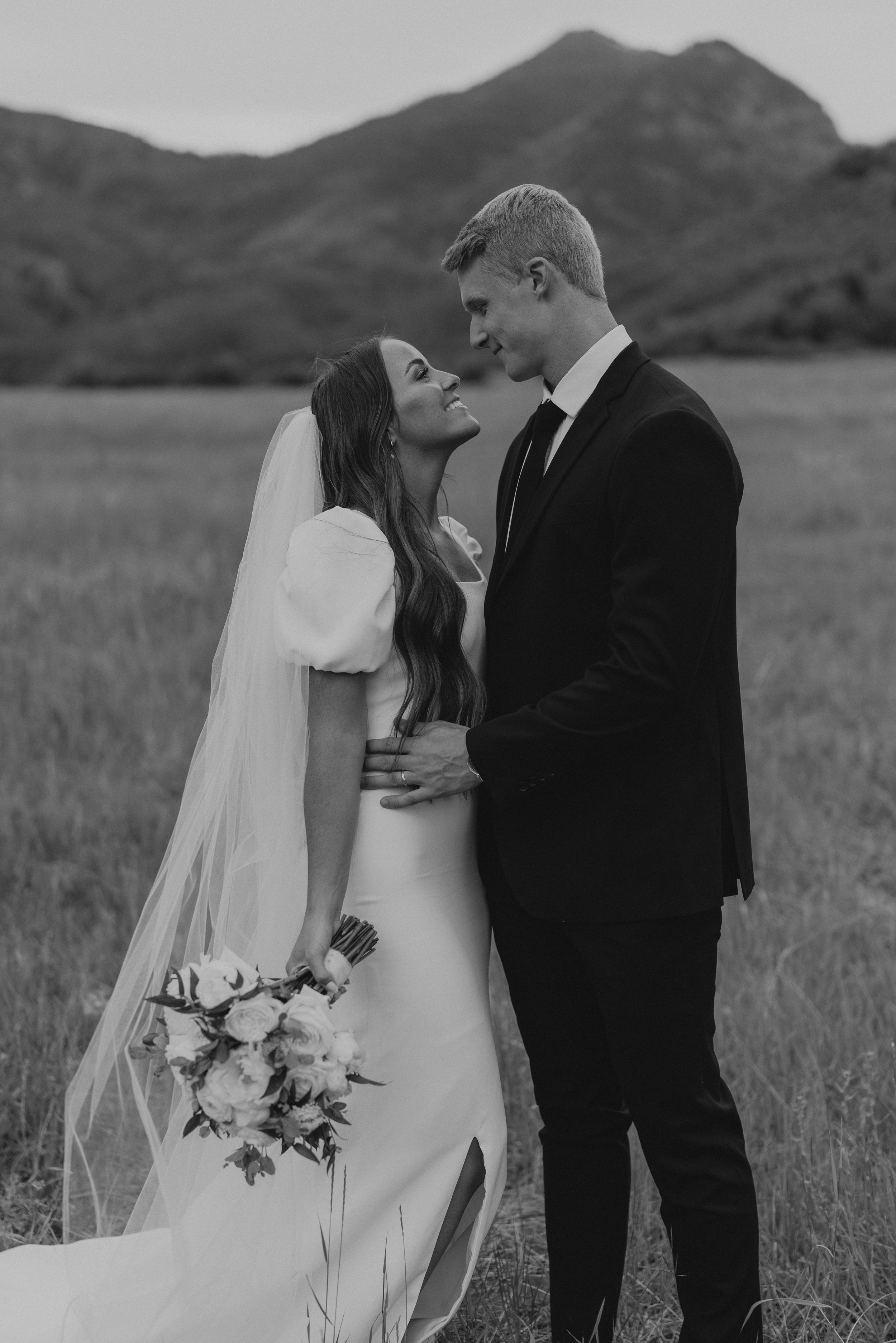 Black and white romantic wedding portrait with mountains and field in background.