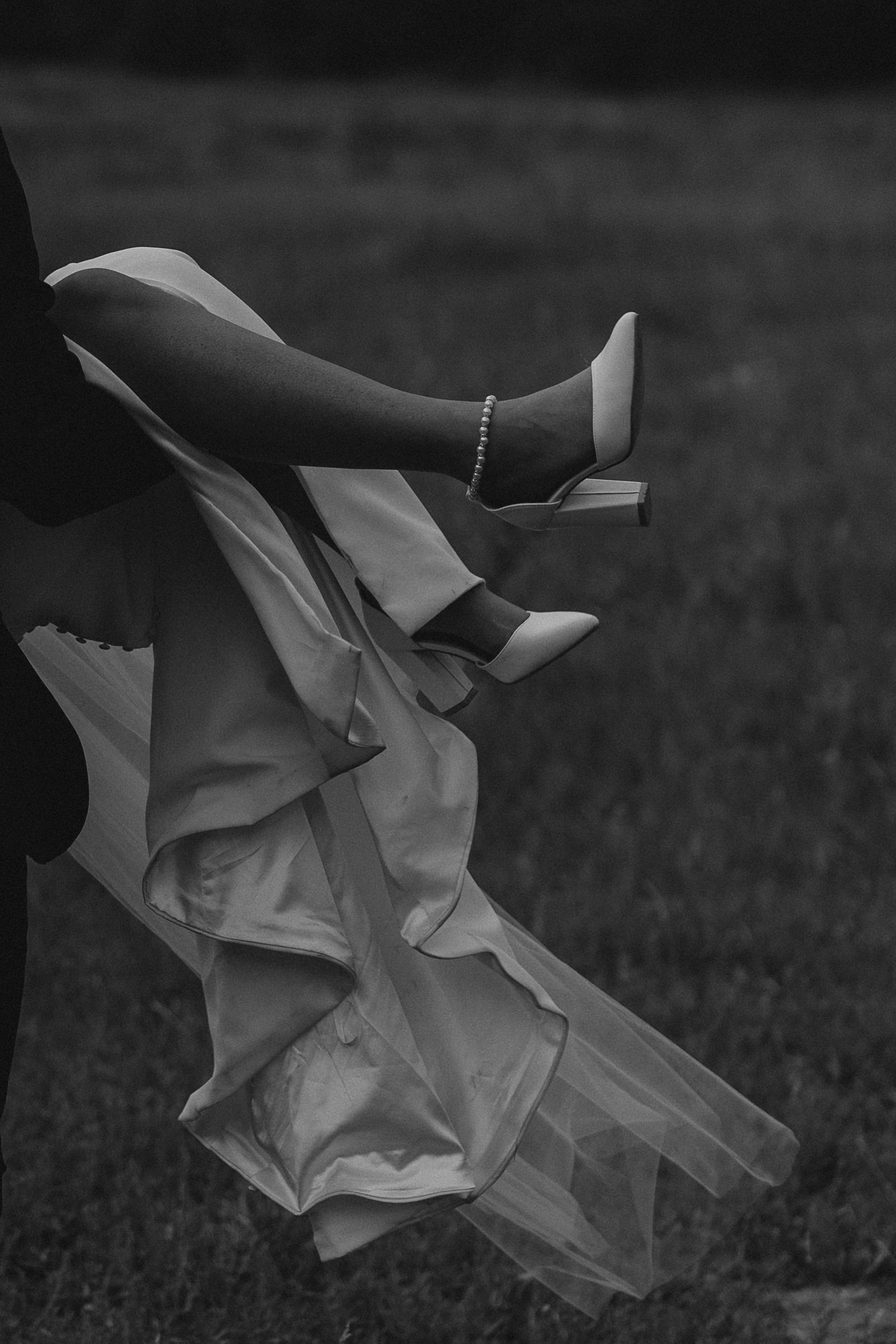 Black and white artistic shot of bride's shoes and flowing dress hem.