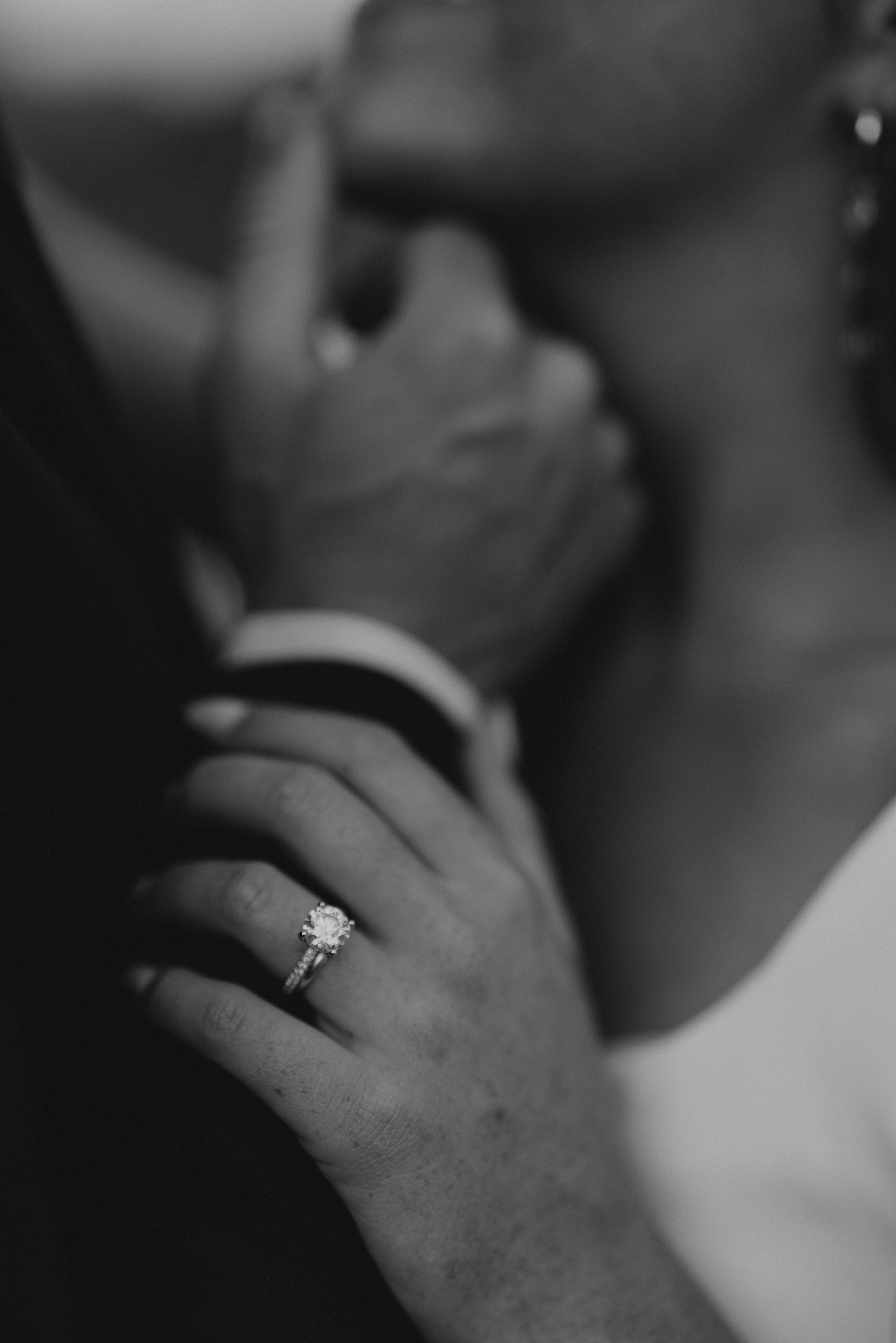Black and white close-up of wedding rings and clasped hands.