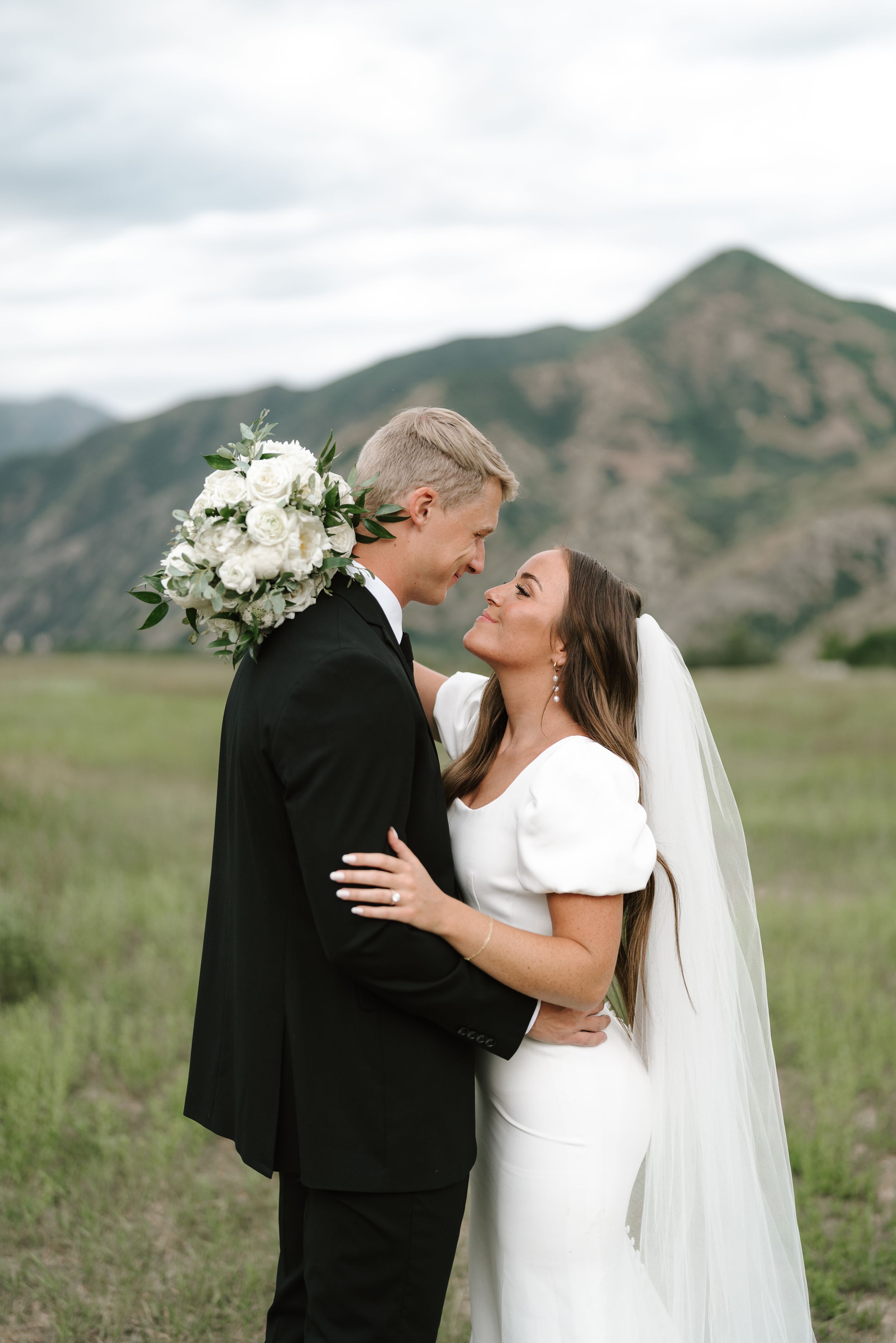 Intimate wedding moment captured against beautiful mountain backdrop with elegant white floral bouquet.