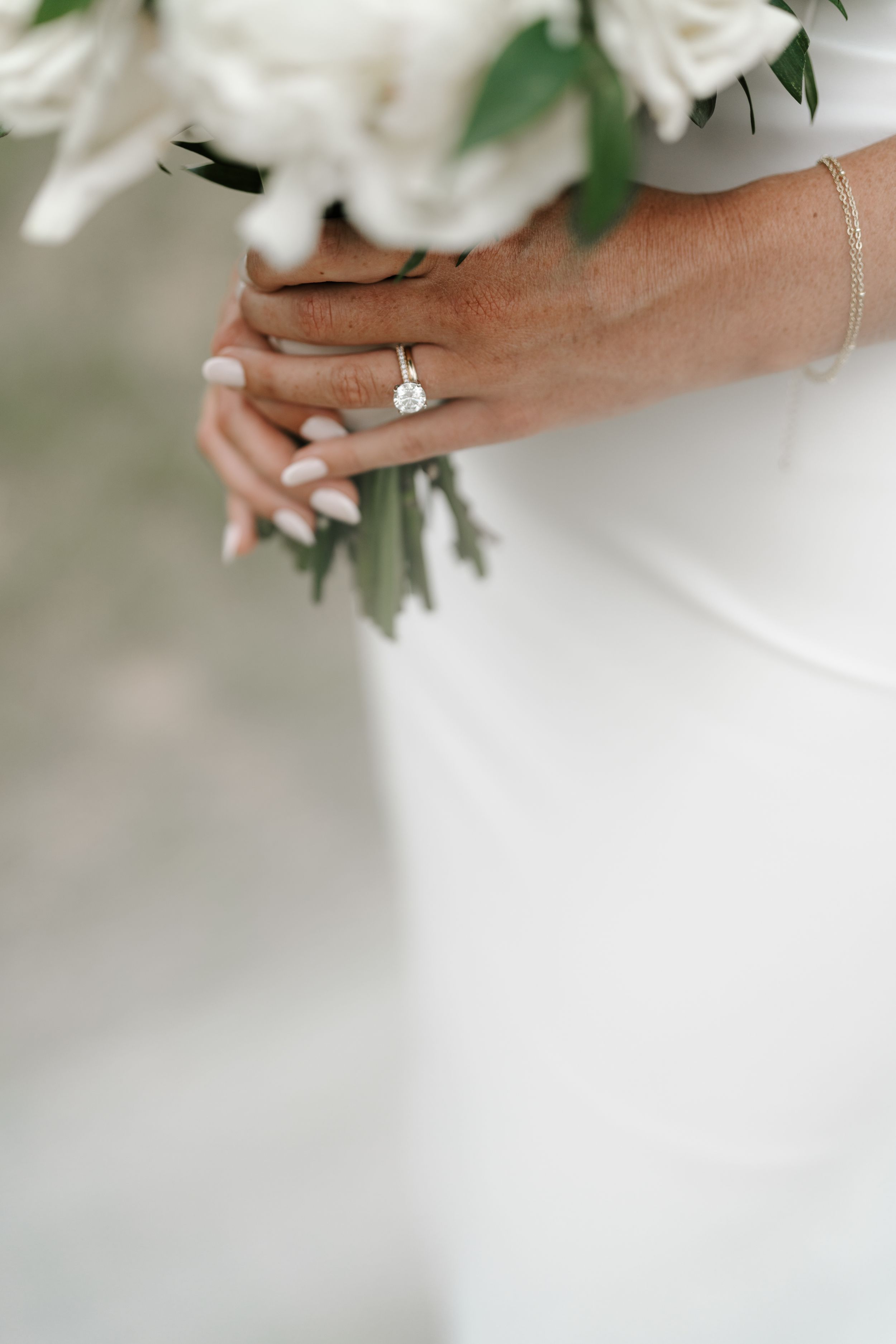Close-up of bride's hand holding white roses showing elegant engagement ring and bracelet.