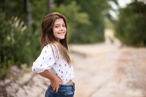 Child portrait of a girl in white floral top and jeans posing on a countryside path.