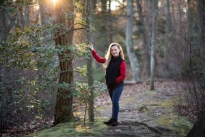 Child portrait of a girl in red jacket and jeans poses in sunlit winter forest in Middletown NJ