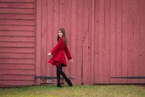 Child portrait of a girl in red dress twirling against a rustic red barn wall in Middletown NJ