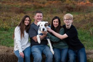 A happy family portrait with their white dog on a hay bale in an autumn field in Monmouth County NJ